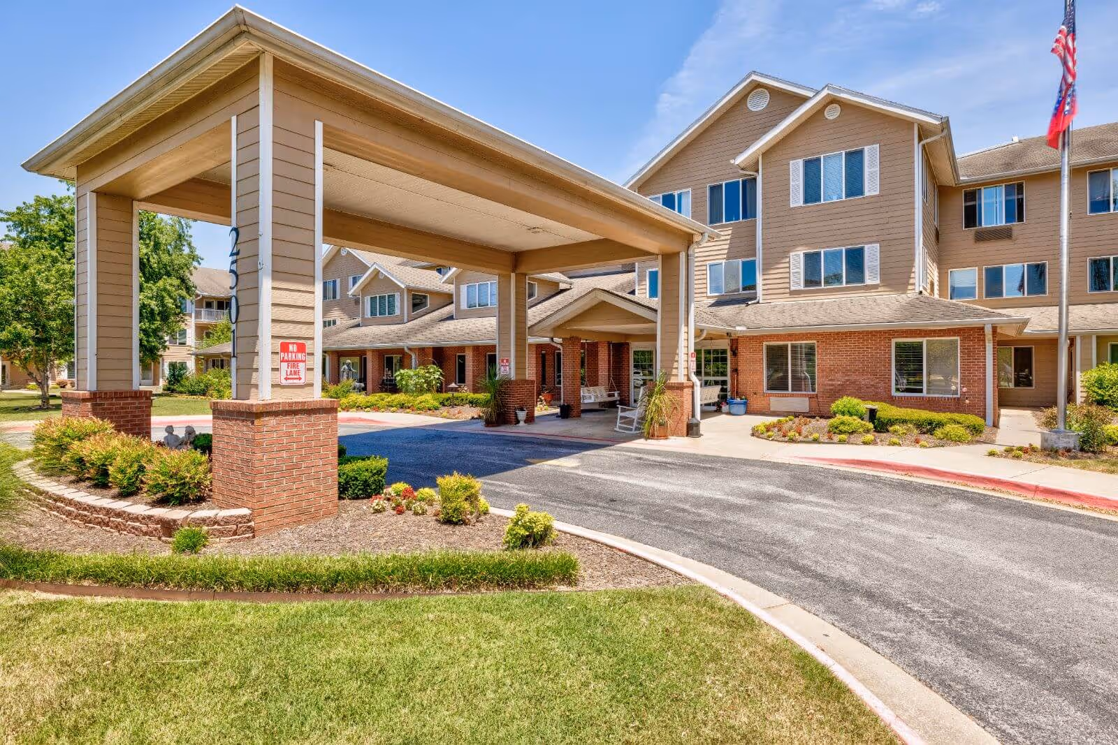 Covered entrance/porte-cochere and driveway of a multi-story senior living facility with landscaped grounds and an American flag.