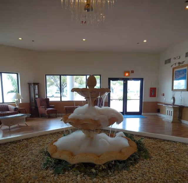 Indoor lobby featuring a three-tiered fountain overflowing with foam in the center, seating areas and double glass doors in the background.