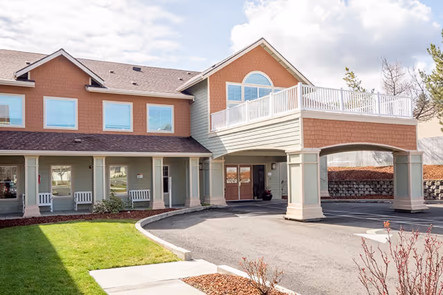 Exterior view of Siskiyou Springs Assisted Living Community building with a covered entrance, multiple windows, and a well-maintained lawn and landscaping in front.