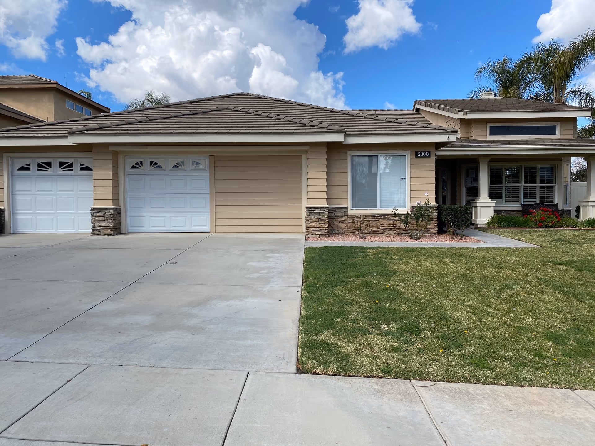 Single-story house exterior with double garages, front porch, and well-kept lawn on a sunny day.