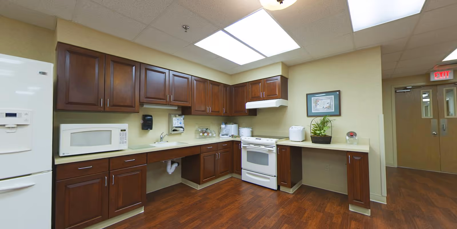 Kitchen area with dark wood cabinets, white refrigerator, microwave and stove, countertops and wood flooring.