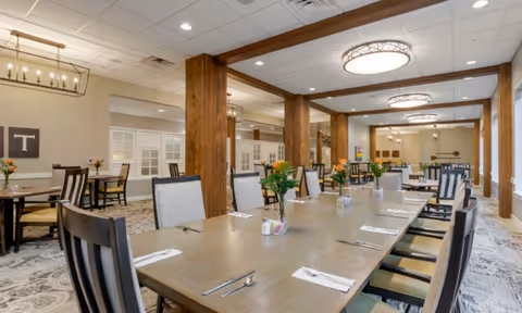 Bright, spacious dining room with long wooden tables set with cutlery and floral centerpieces.