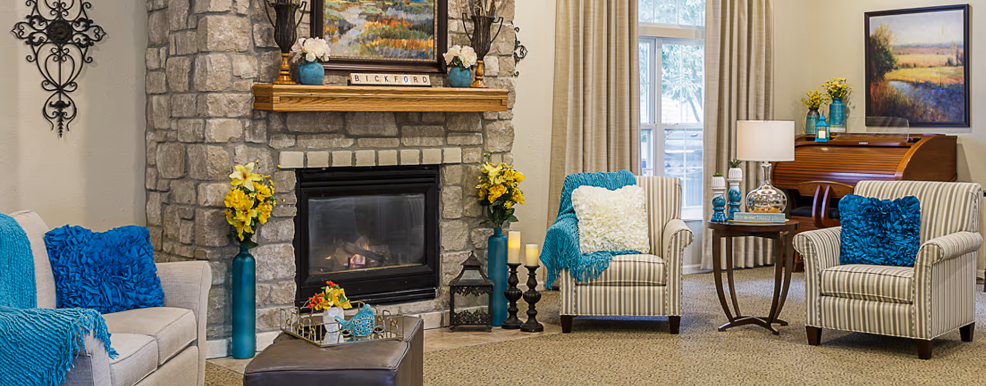 Cozy living room with a stone fireplace, upholstered sofa and armchairs accented by teal pillows and decorative side tables.