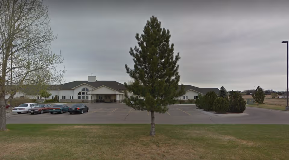 Exterior view of Wel-Life at Scottsbluff with front entrance, parking, and trees.