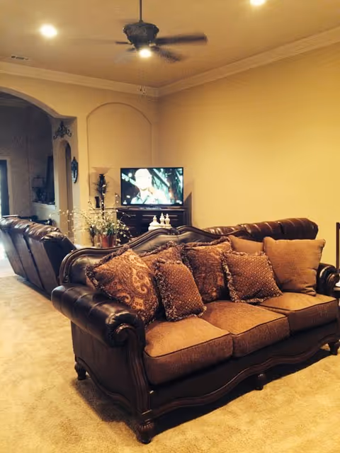 Living room with ornate brown leather-and-fabric sofa and matching loveseat, patterned throw pillows, a ceiling fan, and a TV on a stand.