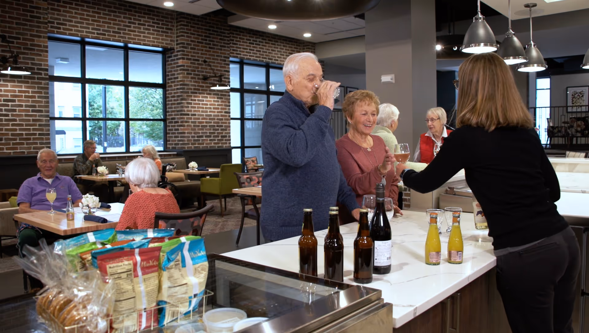 Several senior residents socializing at a service counter and seated at tables in a bright dining area.