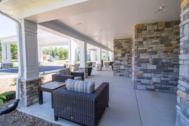 Covered outdoor patio with wicker chairs and stone-clad columns at the facility entrance.