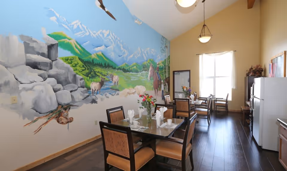 Bright dining room with tables and chairs, floral centerpieces, and a large mountain-and-wildlife mural on one wall.