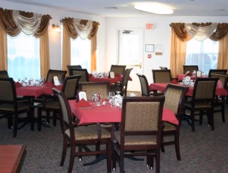 Dining room with multiple tables covered in red tablecloths set with glassware and napkins.