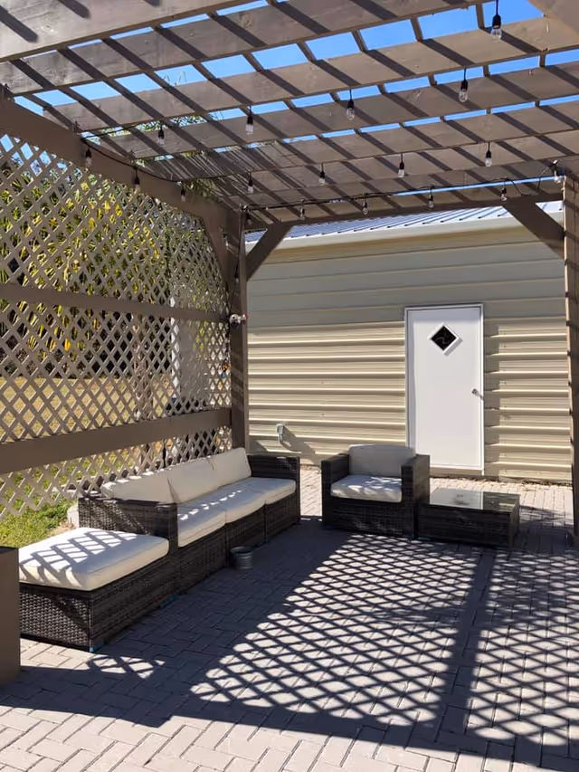 Covered outdoor patio with wicker seating under a lattice pergola casting patterned shadows.