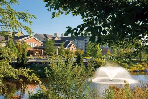 Exterior view of Brooksby Village with a pond fountain, trees, and campus buildings.