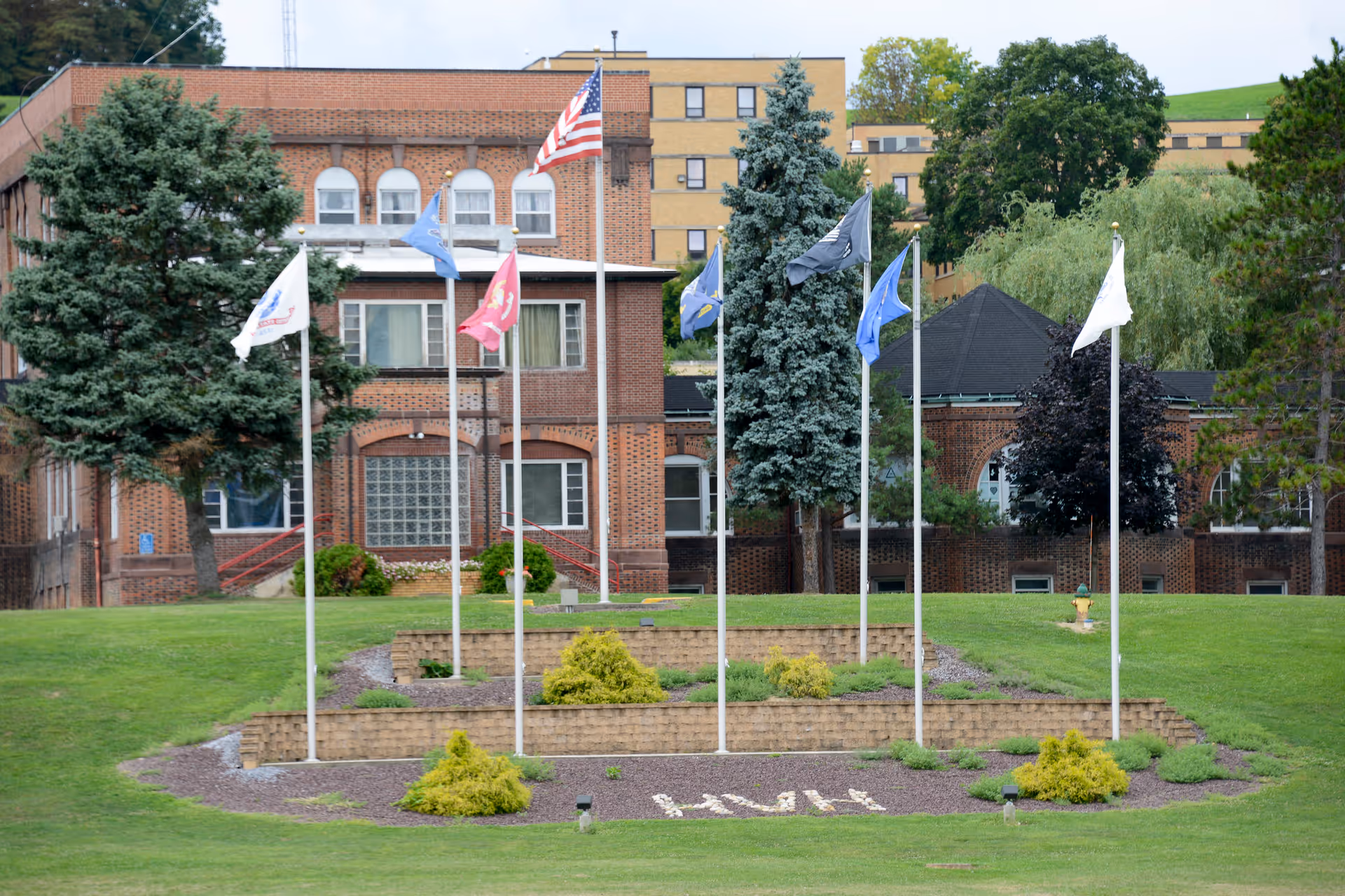Brick veterans home building with multiple flagpoles and terraced landscaped lawn in front.