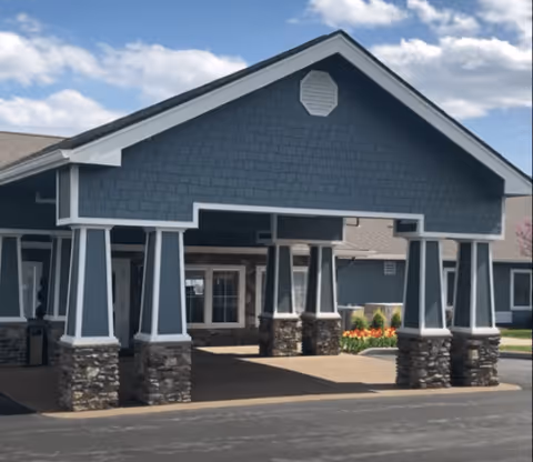 Front exterior view of Barathaven Alzheimer's Special Care Center showing a covered entrance with stone pillars and a blue gabled roof under a partly cloudy sky.