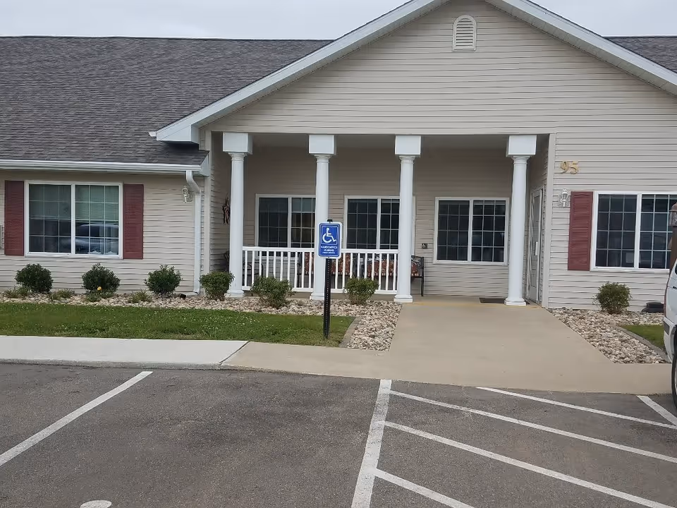 Front entrance of a one-story residential building with a covered porch supported by white columns, an accessible ramp and a handicap parking sign.
