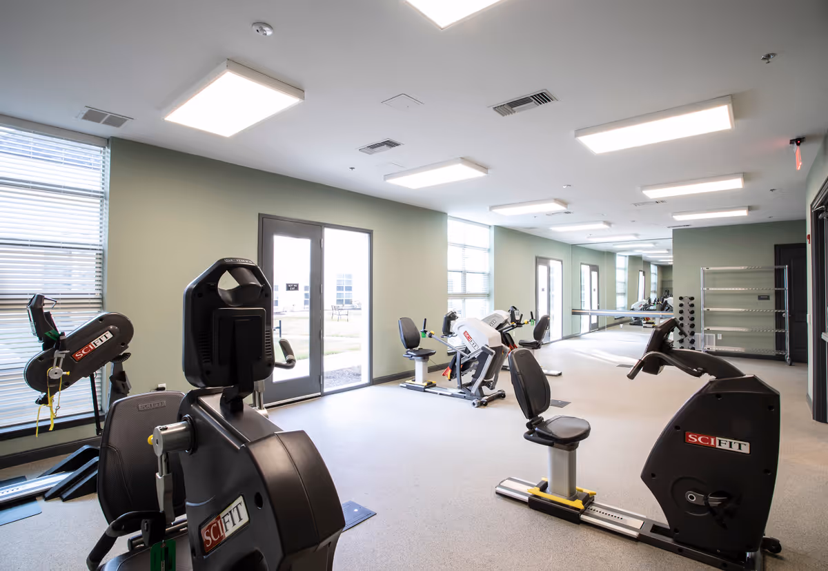 Bright fitness room with recumbent exercise bikes, a mirrored wall, windows, and double doors.