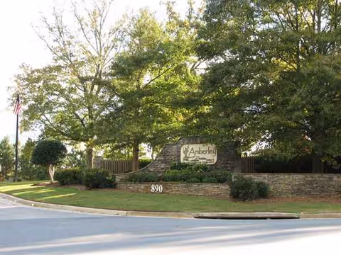 Stone entrance sign for Amberley Senior Community, surrounded by trees and manicured landscaping.