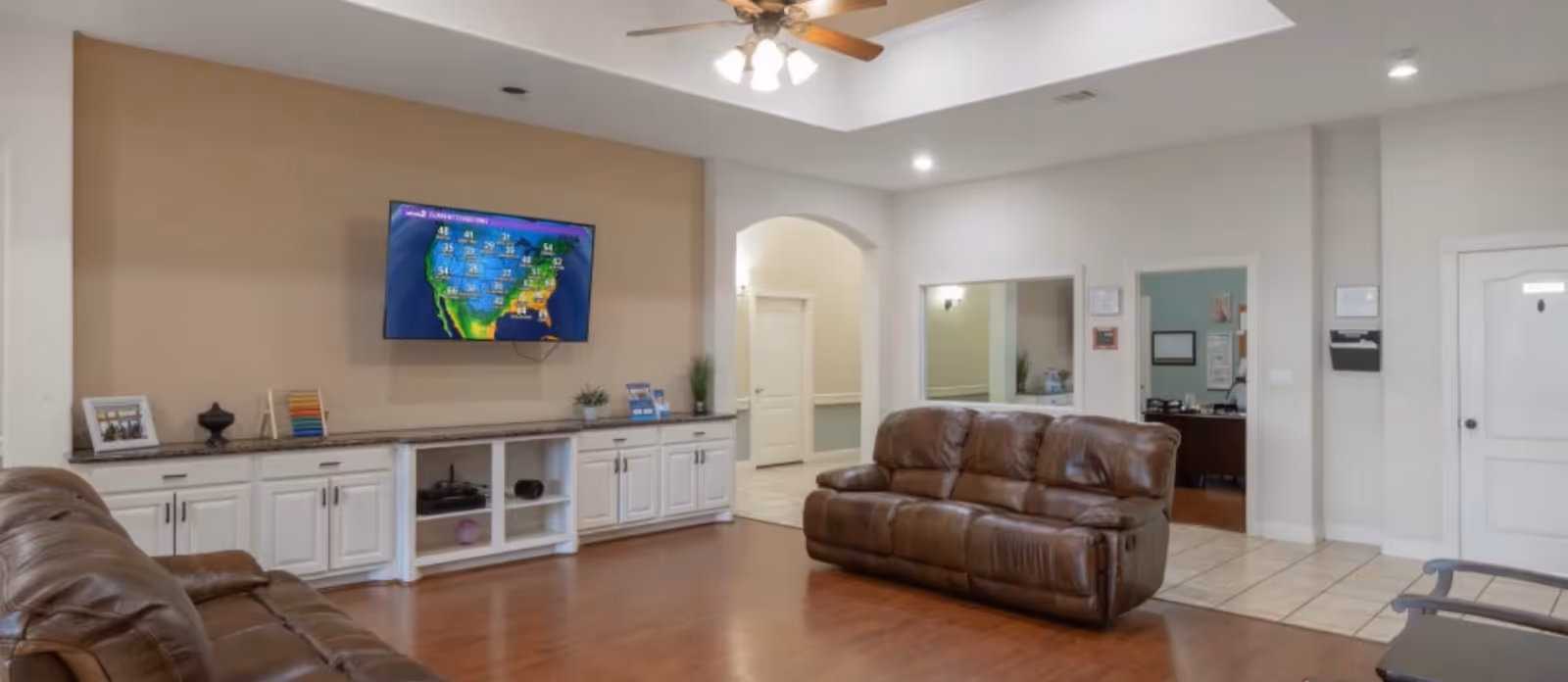 Spacious common room with leather sofas, a wall-mounted TV, and white built-in cabinets.
