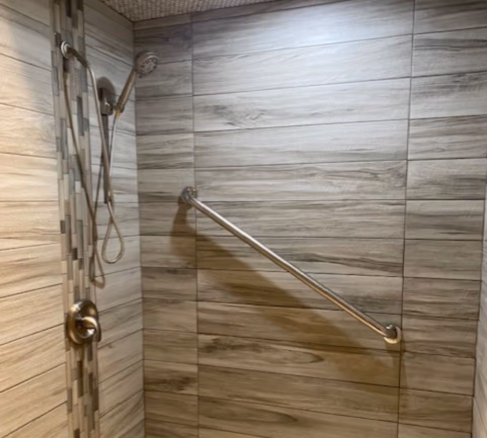 Tiled shower stall with a handheld showerhead and a diagonal stainless steel grab bar.