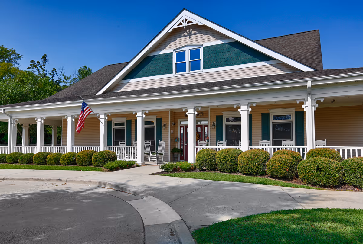 Front view of a one-story senior living facility with covered porch and well-kept shrubs outside.