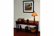 Wooden console table against a beige wall with a table lamp, framed landscape artwork above, and decorative boxes, vases and a basket beneath.