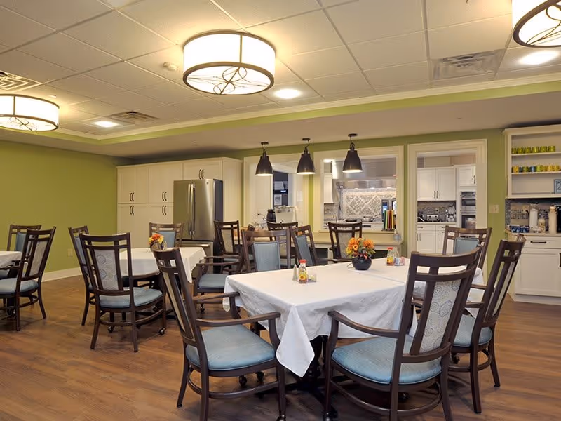 Interior view of the dining room at Park Springs, featuring tables with white tablecloths, wooden chairs, and modern light fixtures.