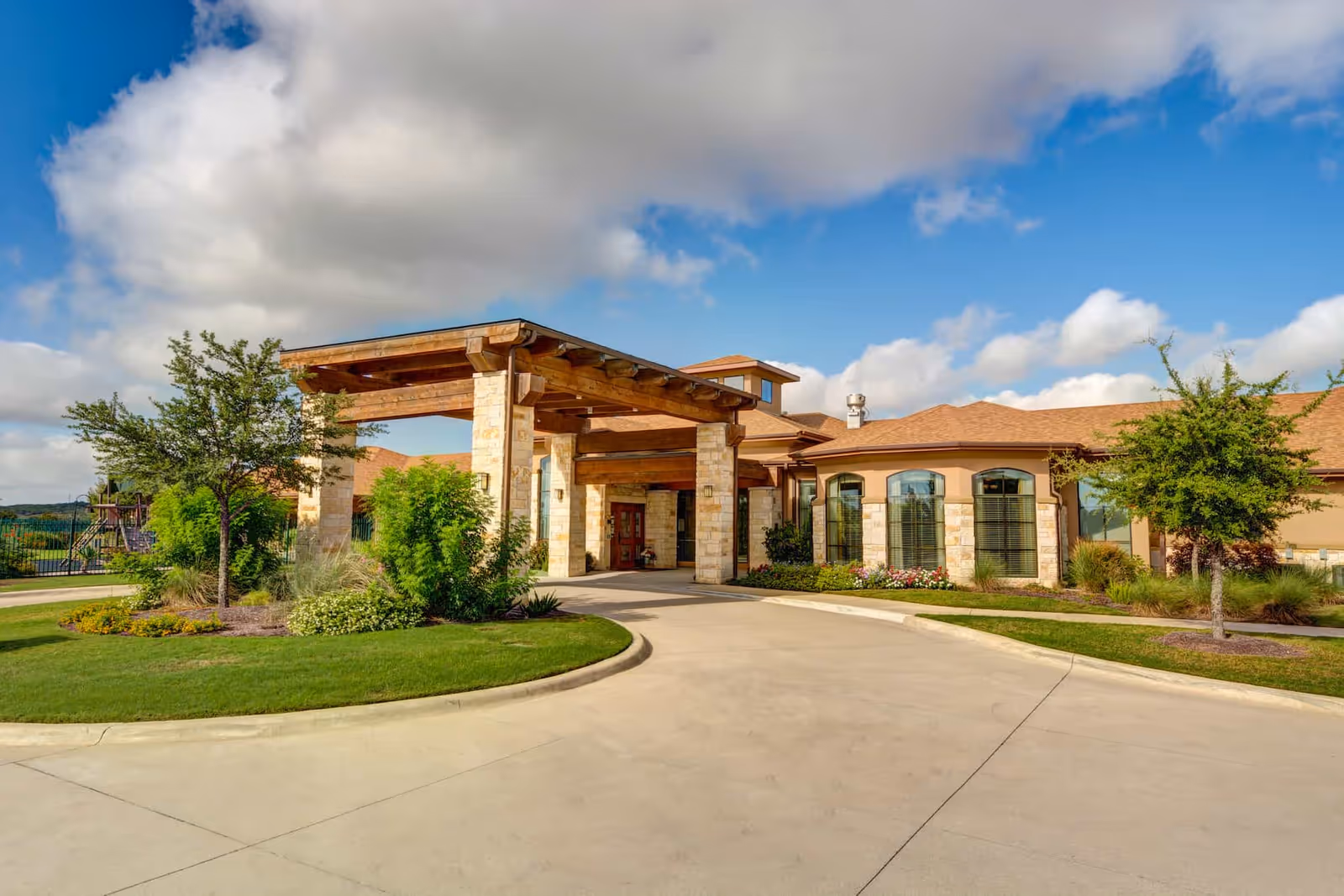 Front entrance and covered porte-cochère of a senior living building with landscaped grounds under a blue sky.