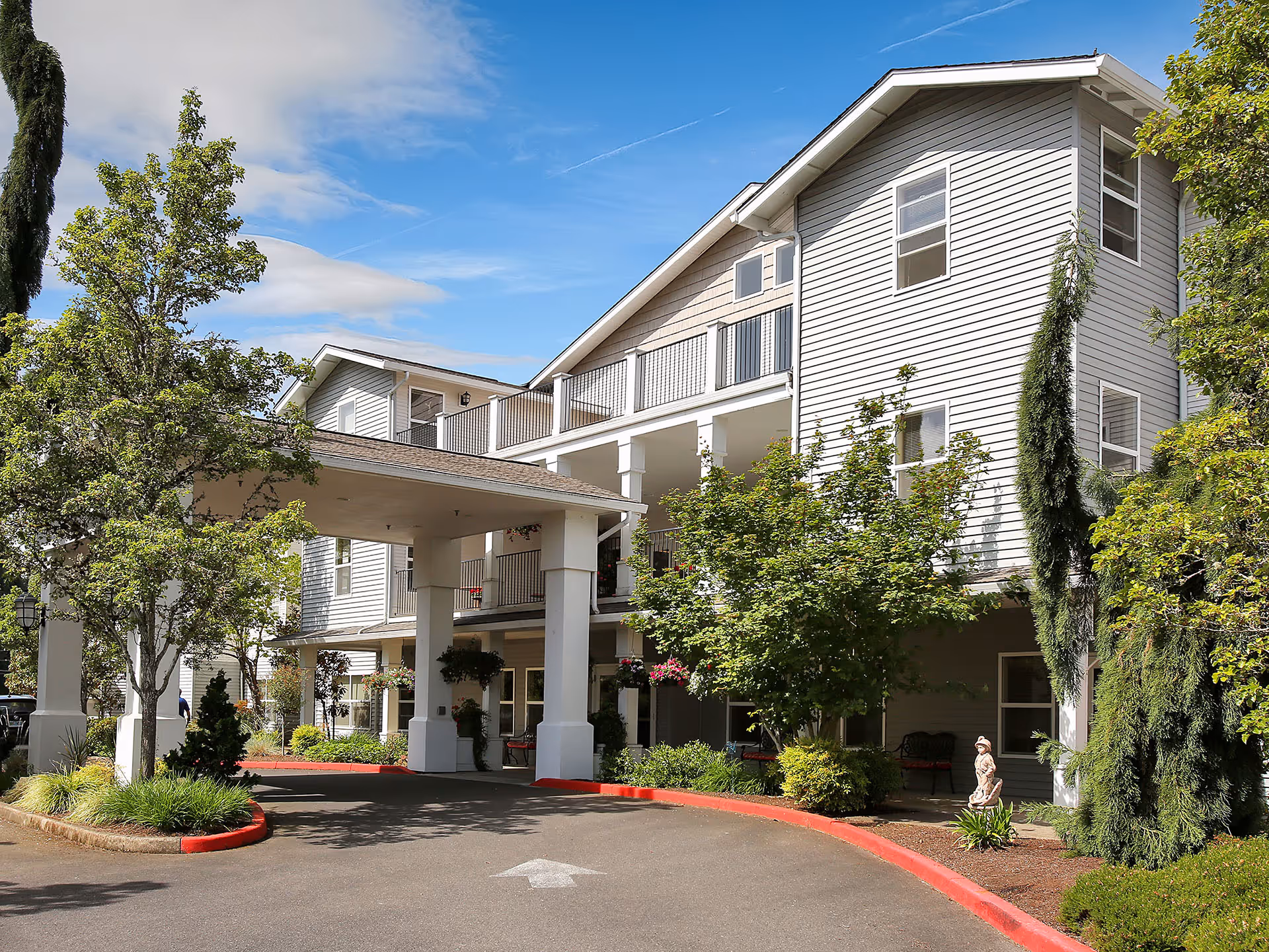 Front entrance of a multi-story senior living building with a covered porte-cochère, balconies, and landscaped grounds.