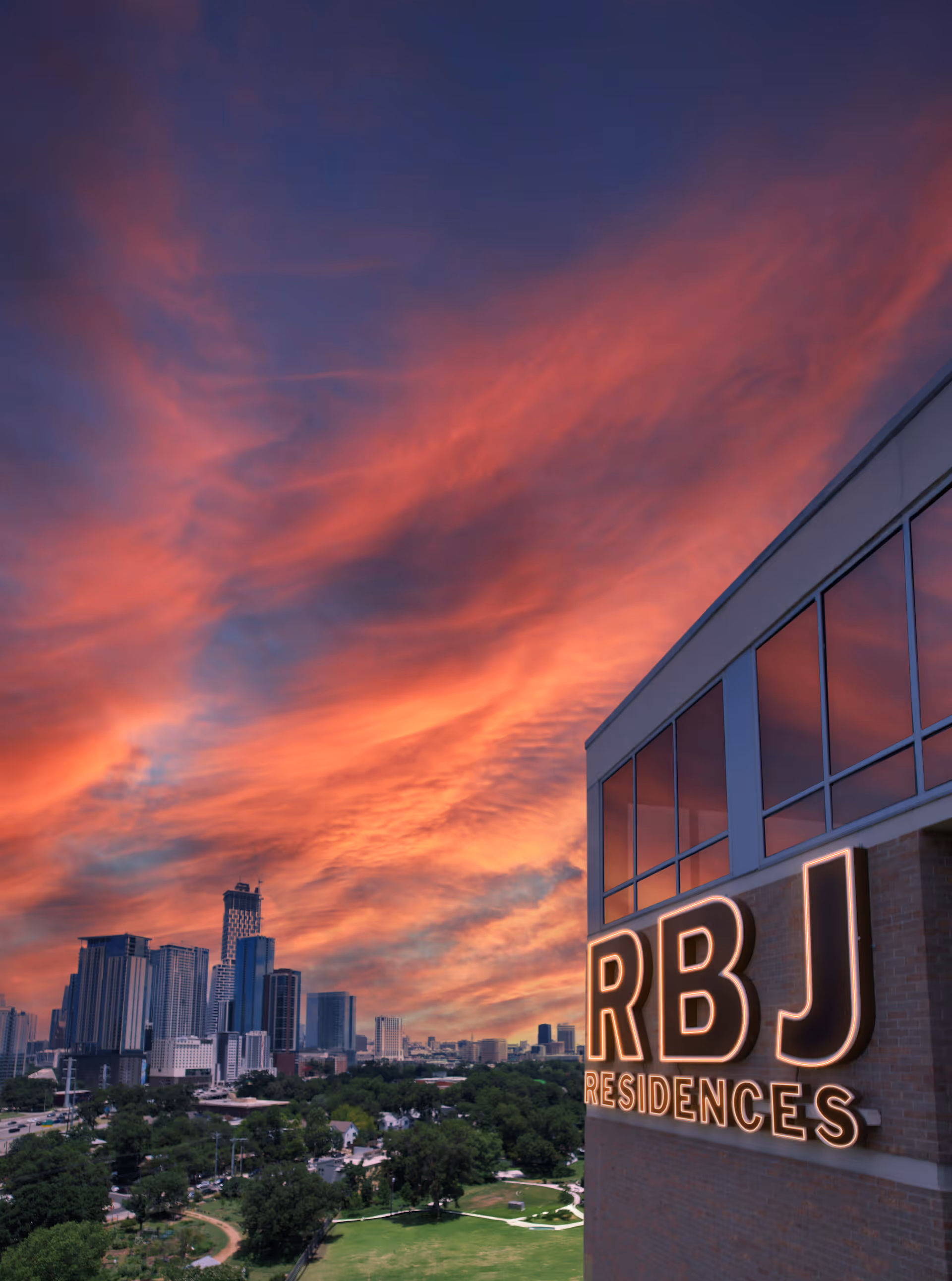 A building exterior with a large RBJ Residences sign against a dramatic sunset and city skyline.