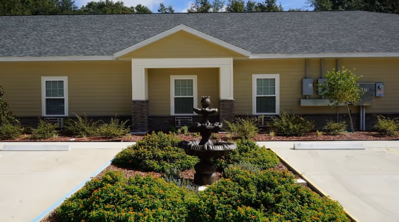 Front exterior of a beige single-story senior living facility with central entrance and fountain.
