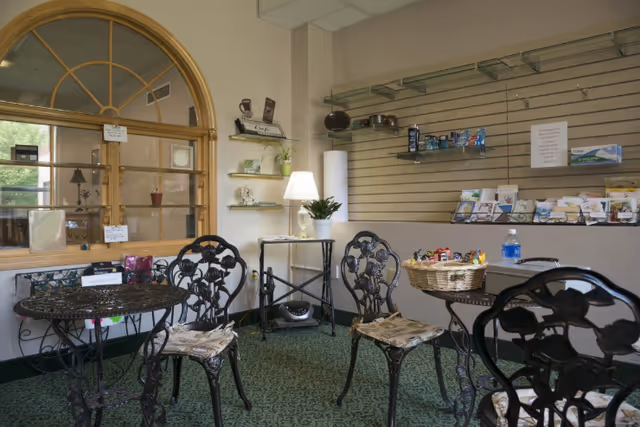 Small interior sitting area with wrought-iron tables and chairs, a lamp, brochure displays, and a reception window.