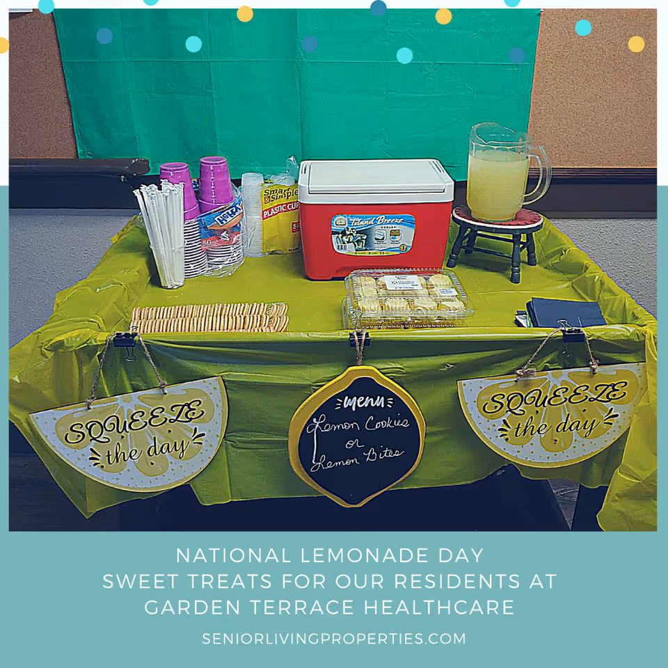 A lemonade-themed refreshment table with plastic cups, a cooler, a pitcher of lemonade, cookies, and lemon-themed signs.