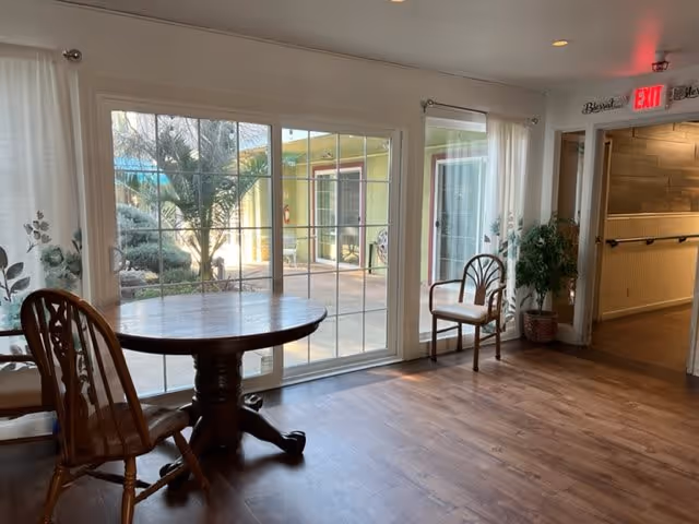 Small dining area with a round wooden table and chairs in front of sliding glass doors overlooking a courtyard.