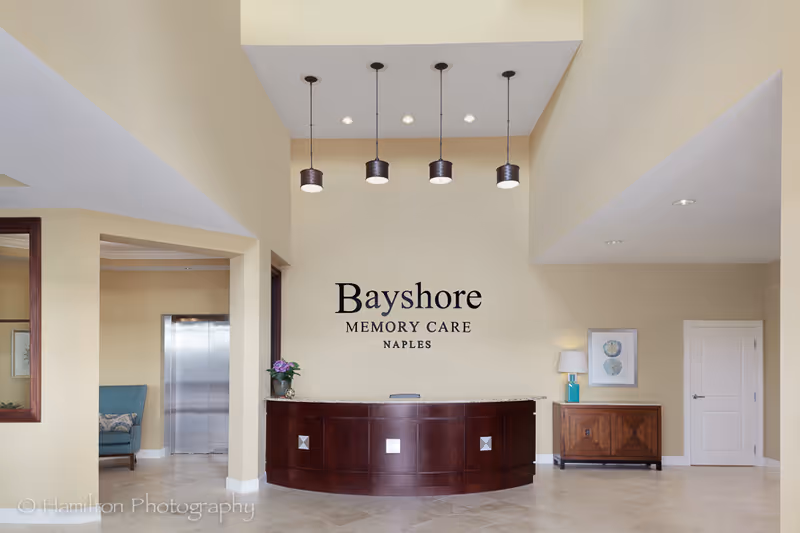 Reception desk and lobby area with 'Bayshore Memory Care' wall signage, pendant lights, and seating.