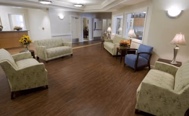 Spacious common seating area with multiple sofas and chairs, wood-look floor, lamps, and a reception desk in the background.