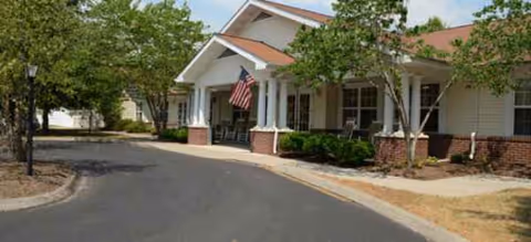 Exterior view of The Groves at Oak Ridge entrance with flag, trees, and driveway.