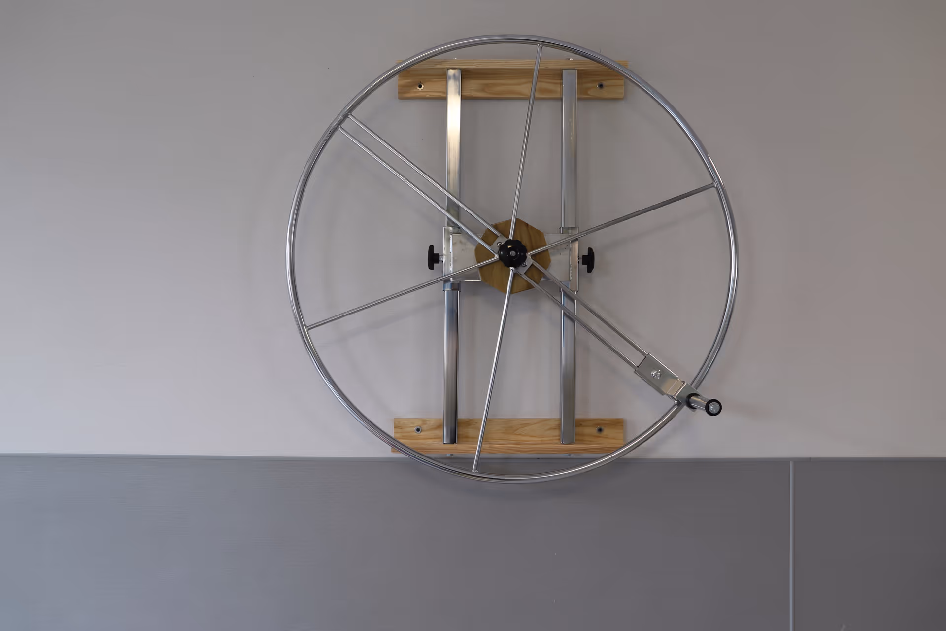 Large metal circular rehabilitation wheel mounted on a pale wall above a gray wainscot.
