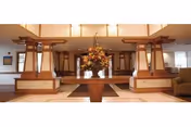 Spacious interior lobby with a central table holding a large floral arrangement, wooden columns, seating areas and warm overhead lighting.