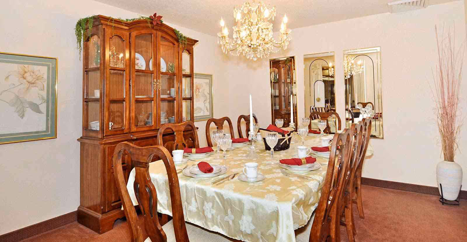 Formal dining room with a long table set for a meal, wooden chairs, a china cabinet, and a chandelier.