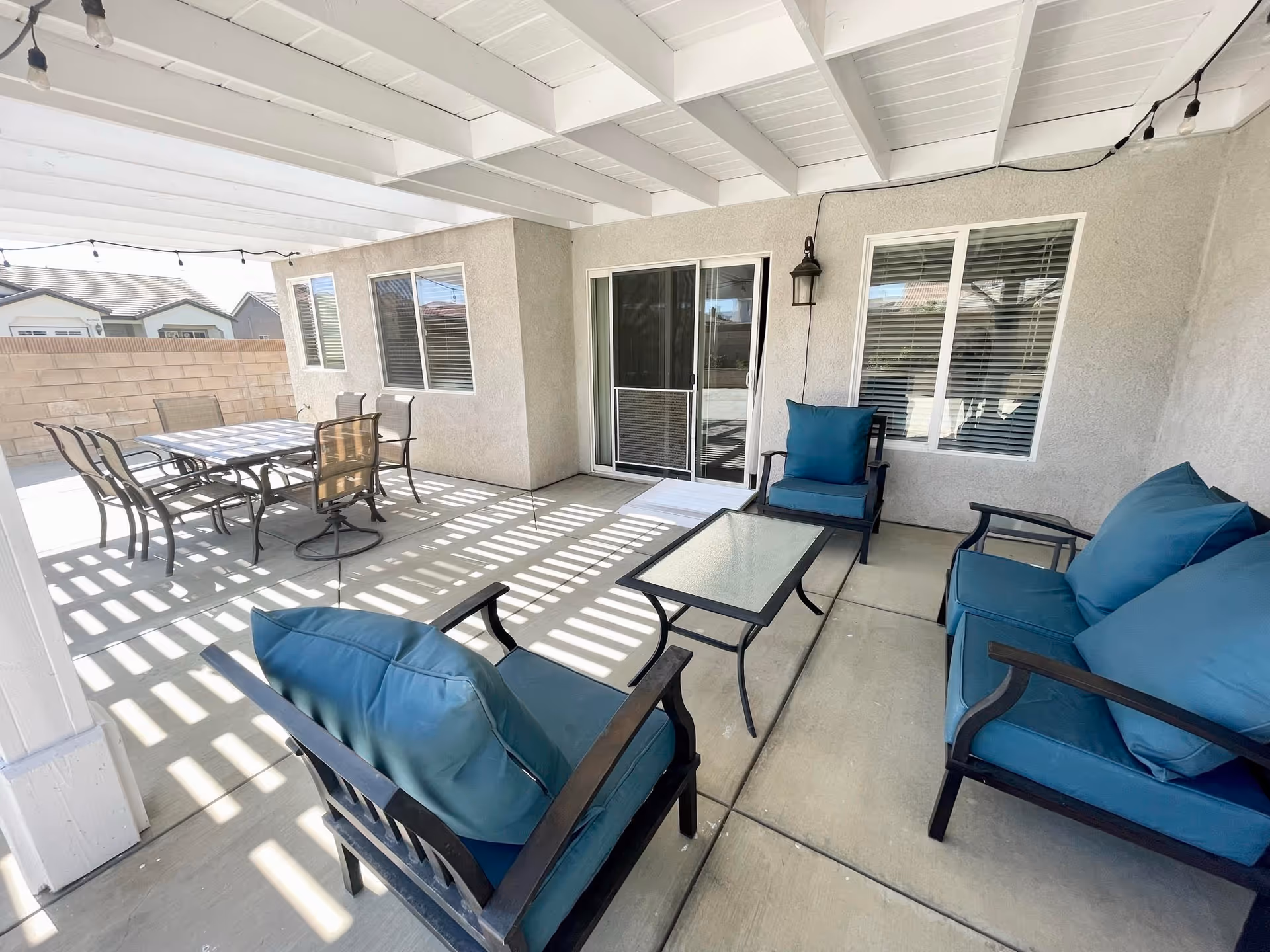 Covered patio with a dining table and blue-cushioned seating under a white pergola.