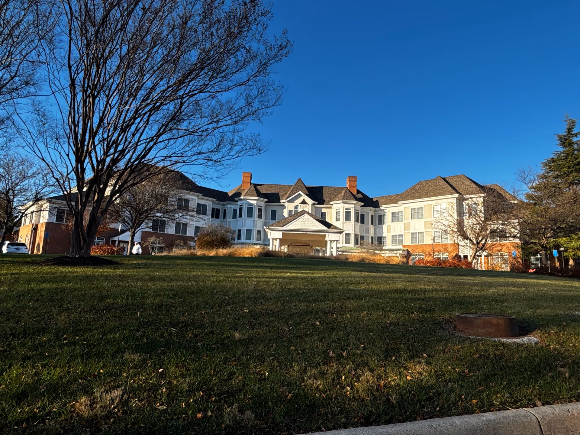 Exterior view of a large senior living facility building named Sunrise at Fair Oaks, with a well-maintained lawn and leafless trees under a clear blue sky.