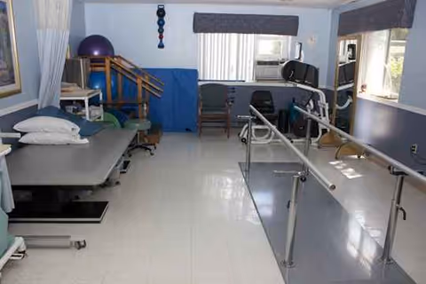 A rehabilitation room with parallel bars, exercise equipment, and mats inside a care facility.