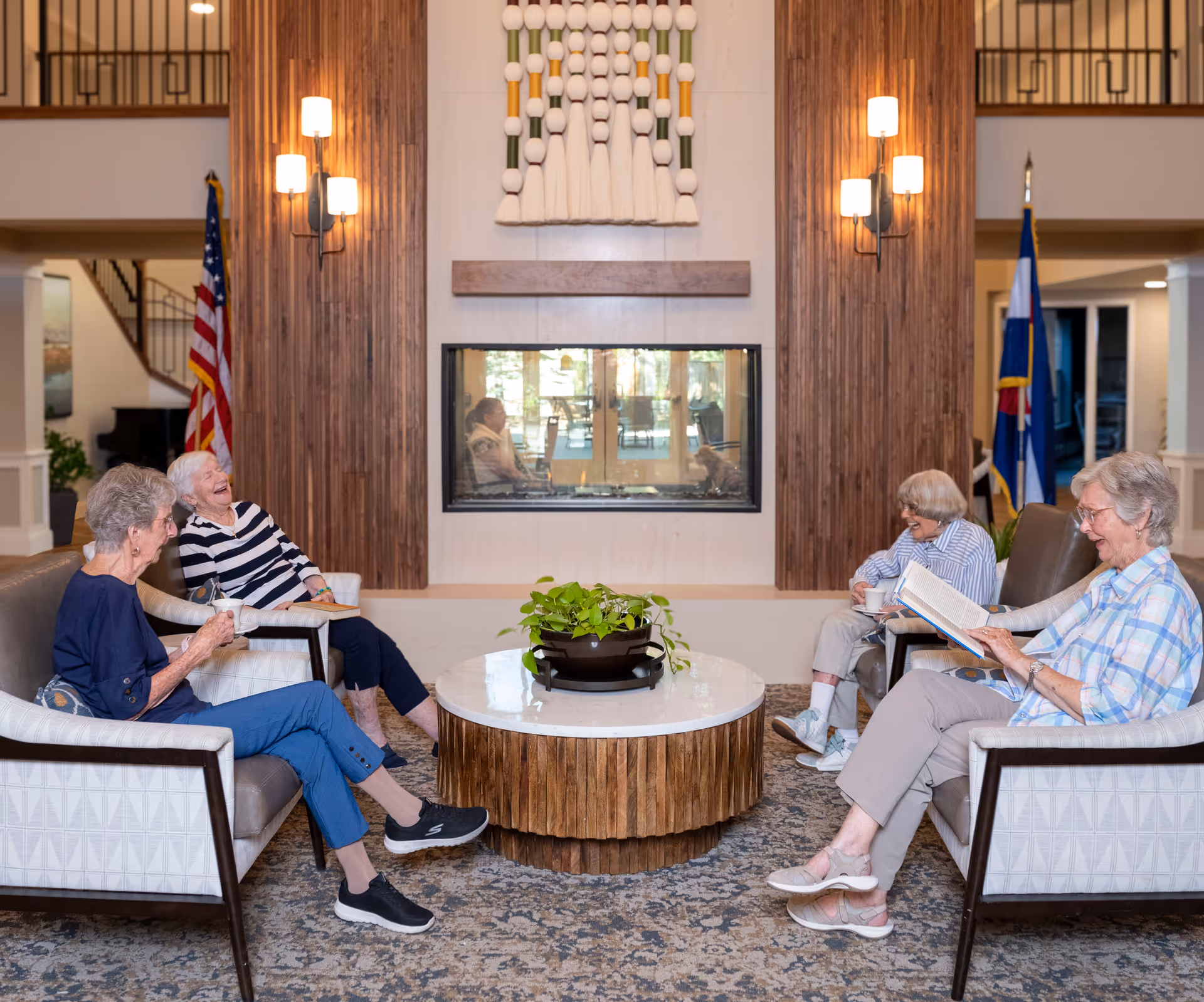 Four elderly women sit and chat around a round coffee table in a bright retirement community lounge.