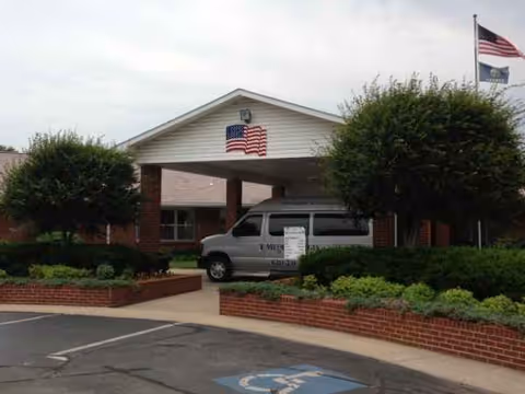 Front view of Medicalodges Frontenac facility with a covered entrance, flags, and a parked van.
