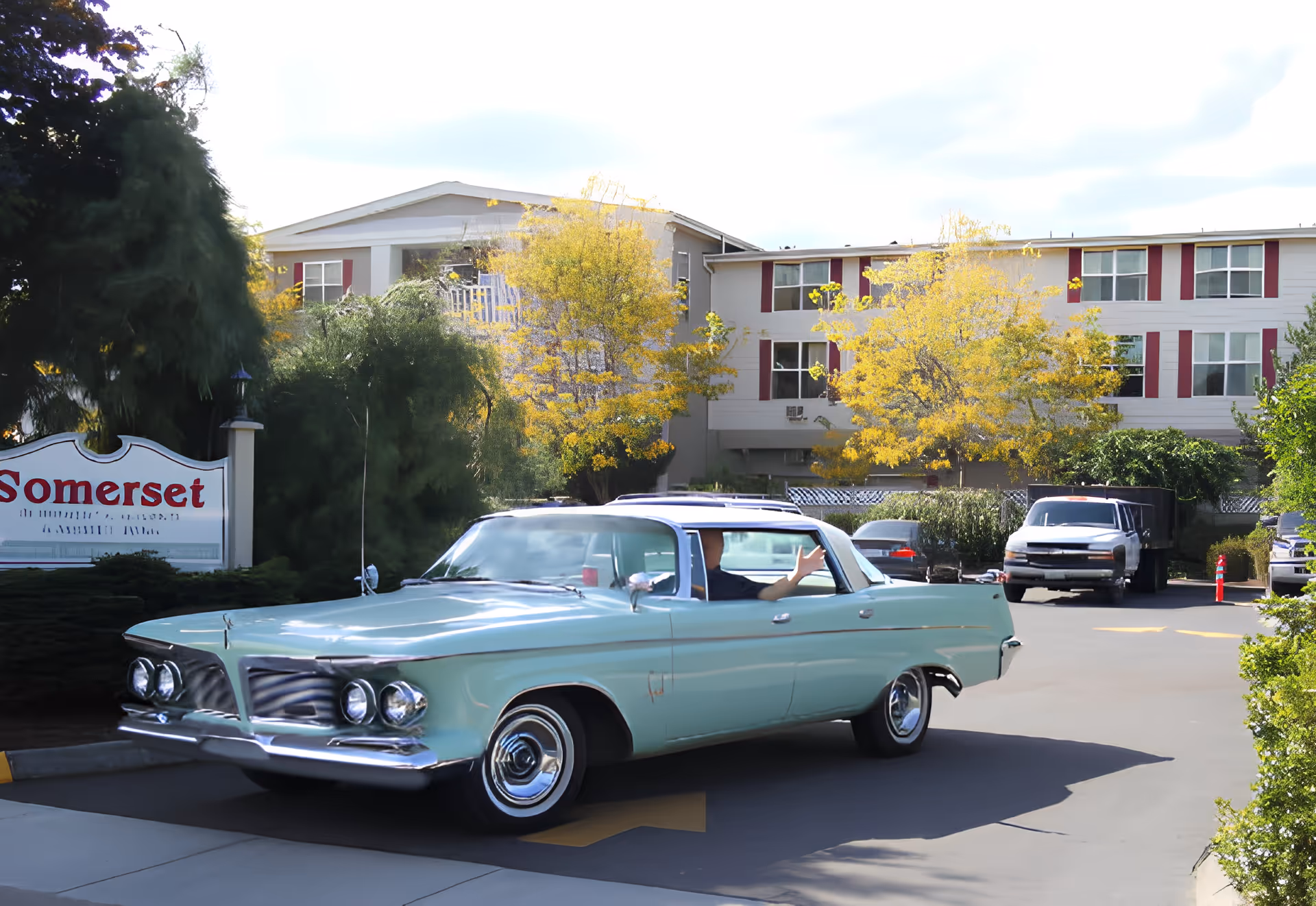A vintage aqua-colored car parked in the driveway in front of the Somerset retirement home building and sign.