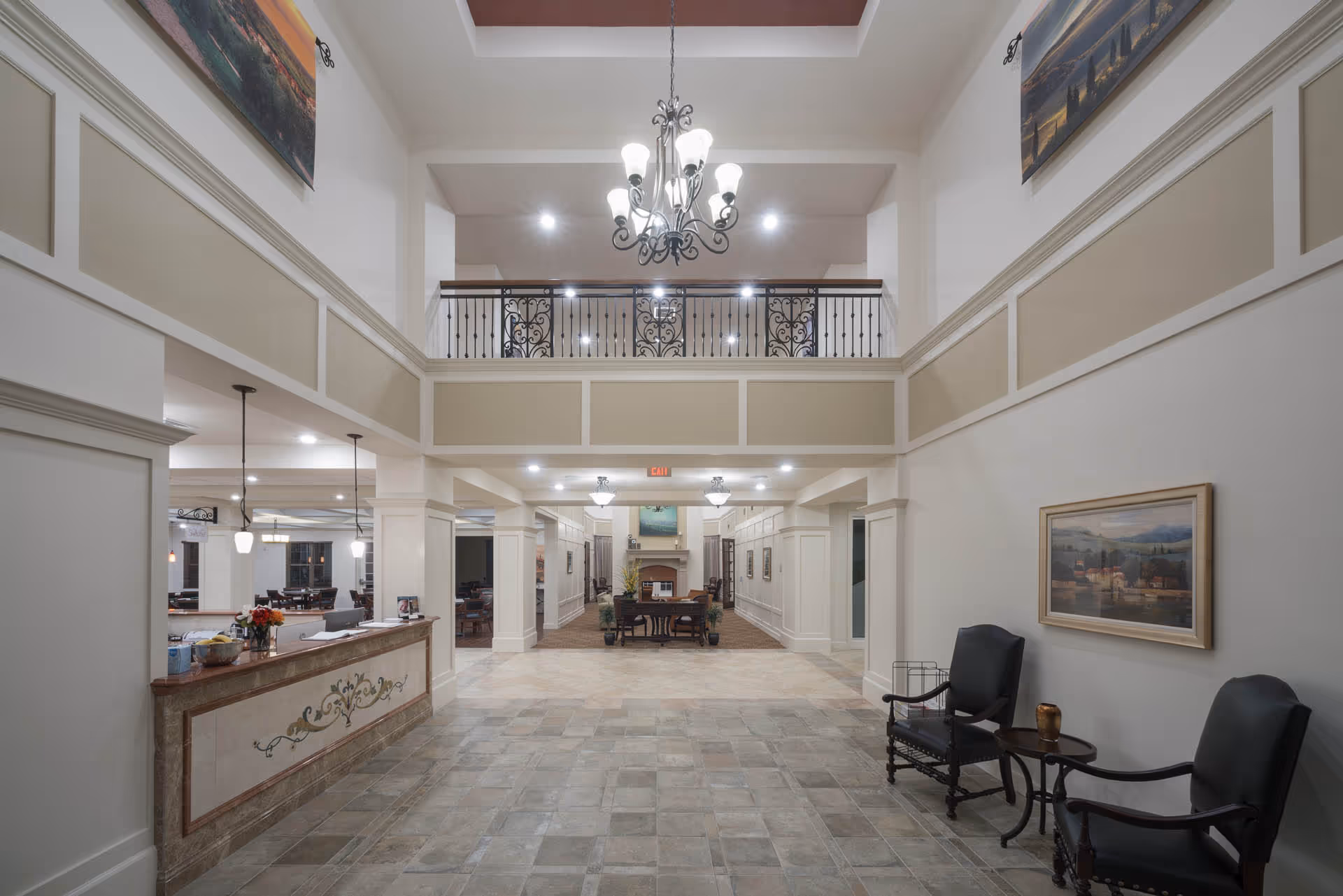 Spacious two-story lobby and reception area with a chandelier, reception desk on the left, seating on the right, and an upper balcony.