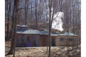 A small wooden building in a forest with a metal roof and chimney.