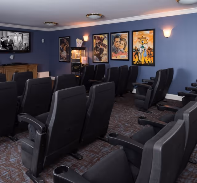 Small screening room with rows of black theater seats facing a TV, vintage movie posters on blue walls, and a popcorn machine.
