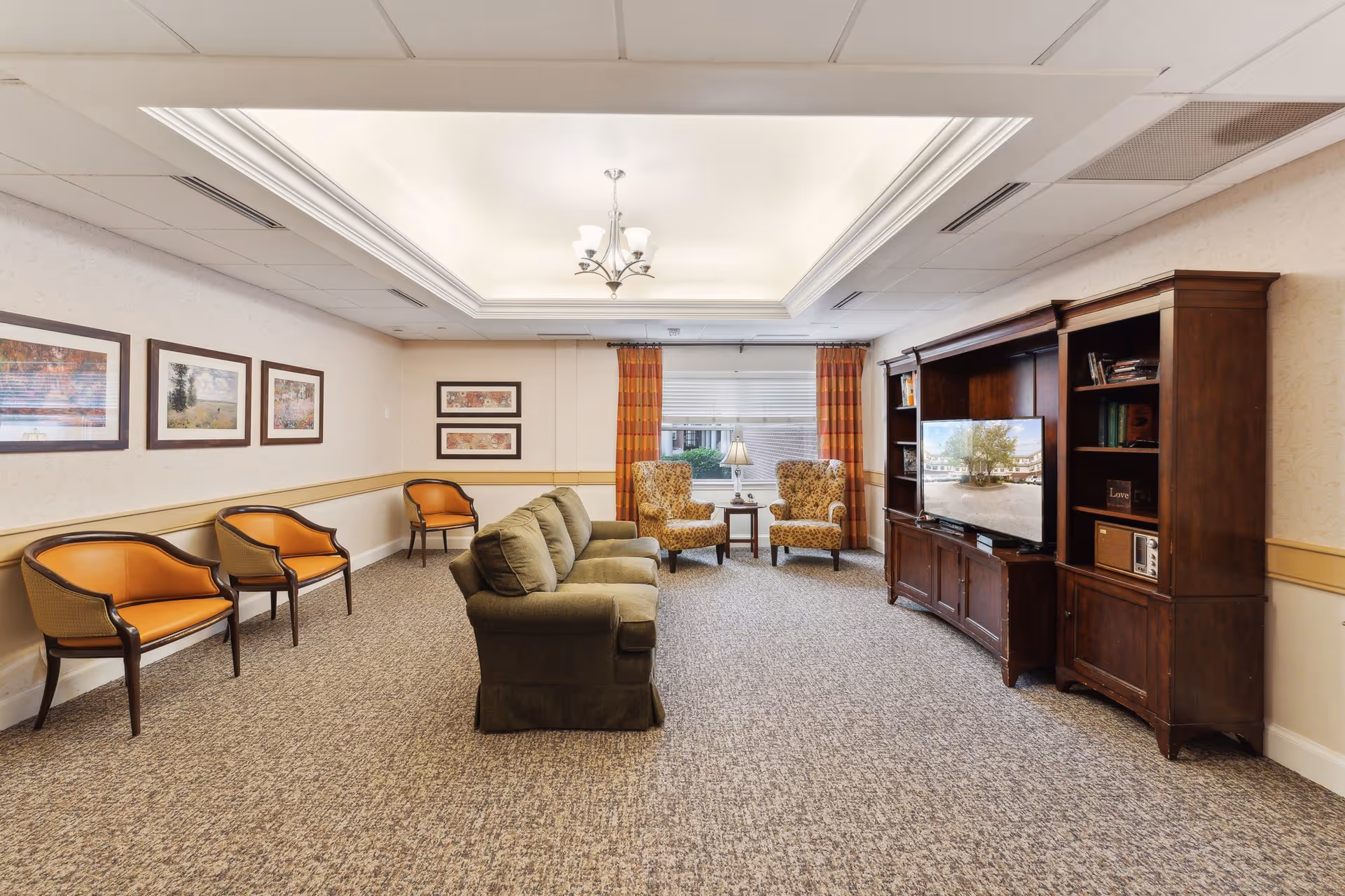 A cozy communal living room with a sofa, several armchairs, a large wooden TV cabinet, and framed artwork.