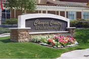 Entrance stone sign reading 'Canyon Country Senior Apartments' surrounded by flowers and lawn with the building in the background.