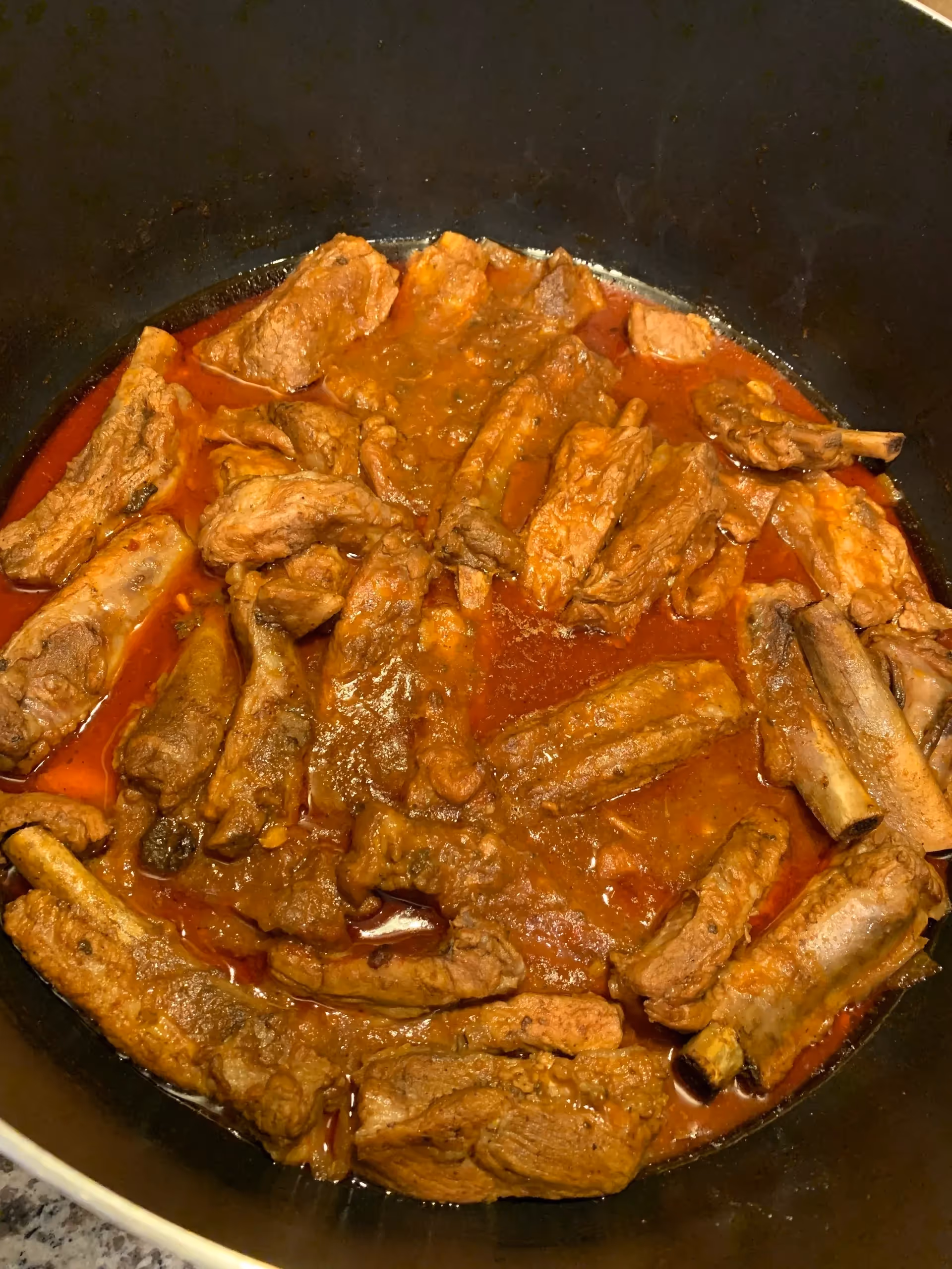 A pot of beef stew simmering in a reddish tomato sauce.